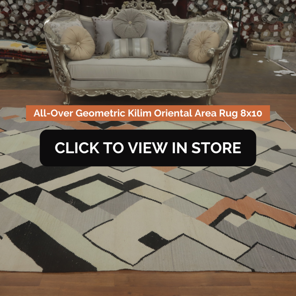 All-Over Geometric Kilim Oriental Area Rug 8x10
A modern, geometric-patterned kilim rug in soft tones of black, cream, orange, and gray is placed in front of an ornate silver and beige couch. Rolls of rugs and a showroom setting are visible in the background.