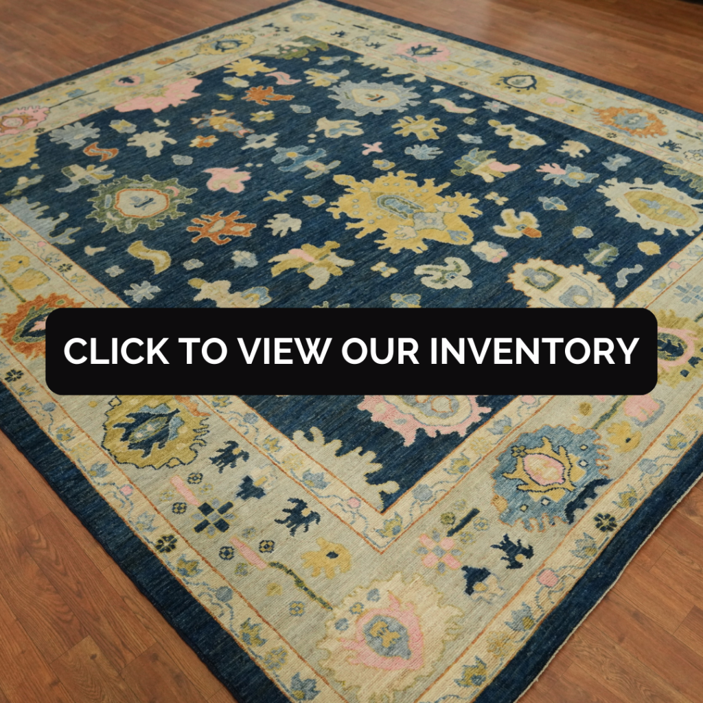 Handmade Blue Oushak Vegetable Dye Area Rug 8x10 This rich blue Oushak rug features traditional floral motifs in gold, peach, and ivory, set against a deep navy background. It lies on a wooden floor in a showroom setting.
