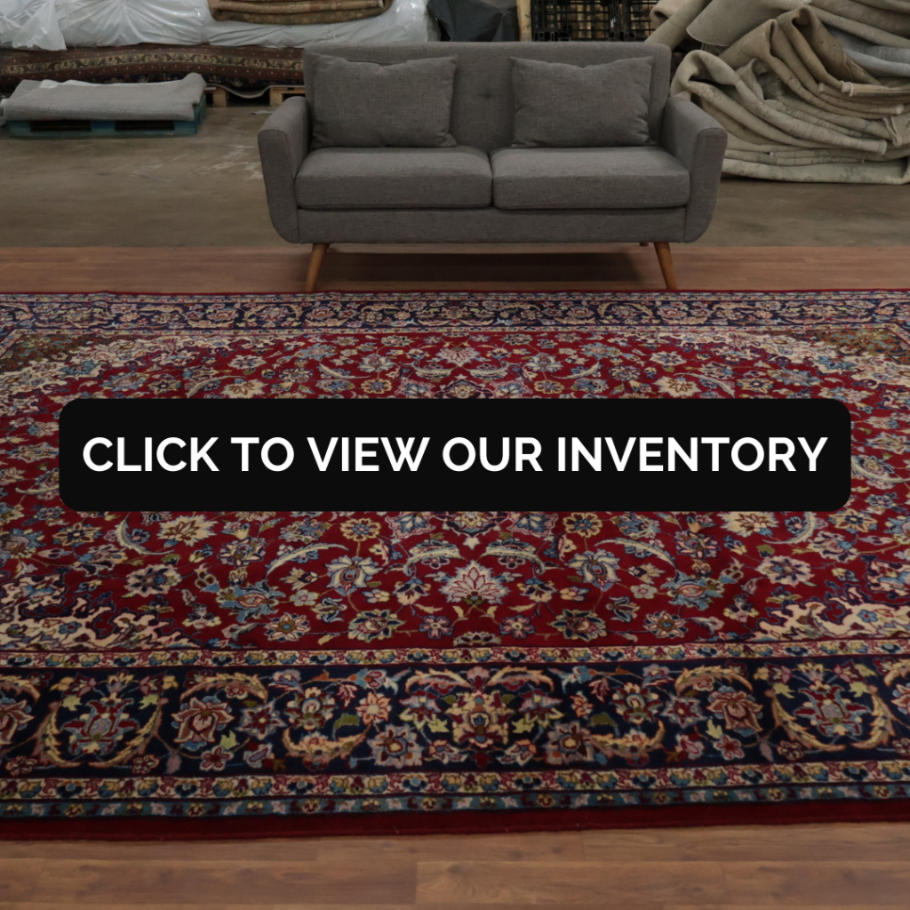 A traditional red Persian rug with intricate floral designs sits in front of a gray sofa in a showroom.