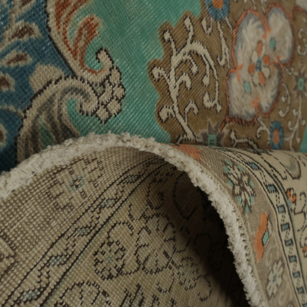Another close-up of the same ornate rug with teal, tan, and beige designs, showing its thickness and detailed floral motifs.