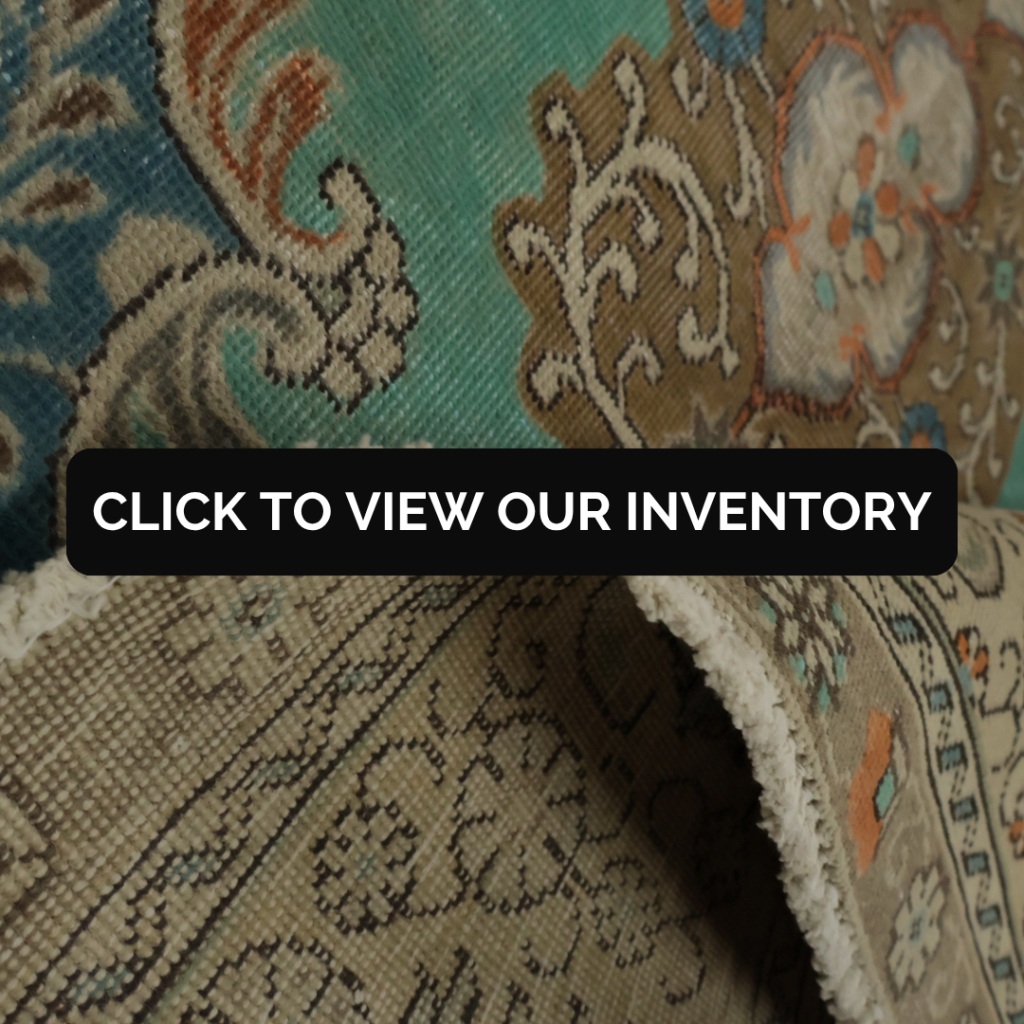 A close-up of a traditional woven rug featuring teal, tan, and beige tones with ornate floral and scroll patterns. One edge is folded to show the detailed design and texture.