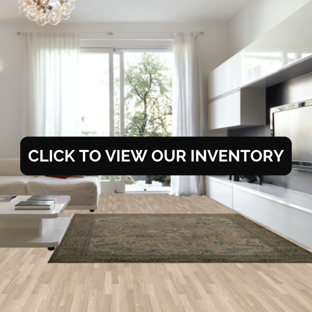 A bright, modern living room with floor-to-ceiling windows and white furniture, styled with a muted green and beige patterned rug that anchors the space. Text overlay reads “Click to view our inventory.”