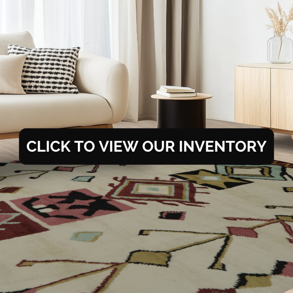 A contemporary living room with a cream sofa, black side table, and minimalist décor. The rug features a cream base with bold geometric patterns in red, black, and gold. Text overlay reads “Click to view our inventory.”