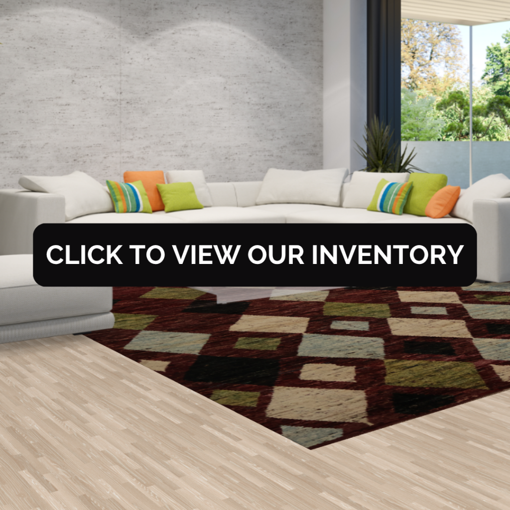 A modern space with a white sectional sofa decorated with colorful throw pillows. The rug has a bold geometric design with deep red, green, and beige squares. Text overlay reads “Click to view our inventory.”