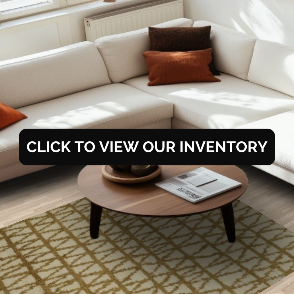 A sunlit room with a white sectional sofa and orange accent pillows surrounding a round wooden coffee table. A beige rug with a crisscross pattern anchors the space.