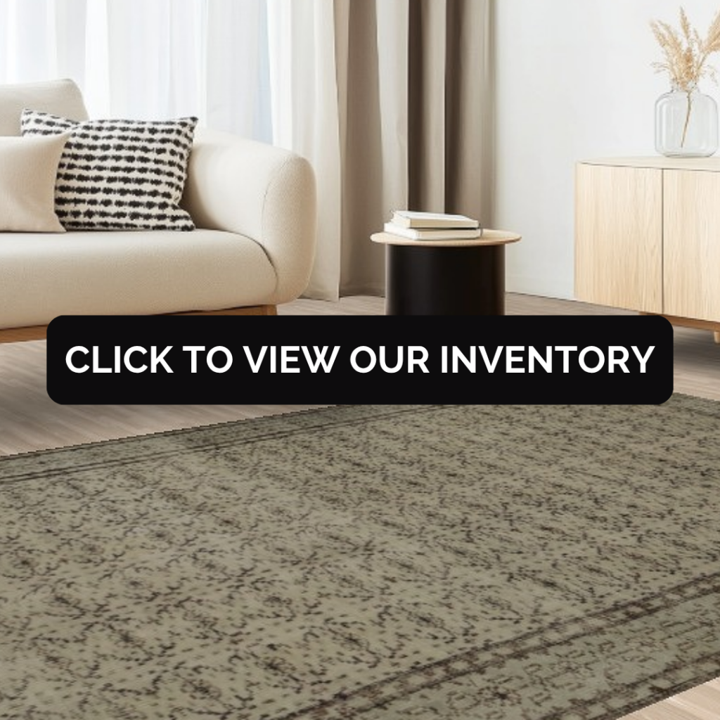 A soft neutral living room with a beige sofa and a distressed gray area rug featuring faint floral patterns and a dark border. The bold black text overlay invites viewers to browse the collection.