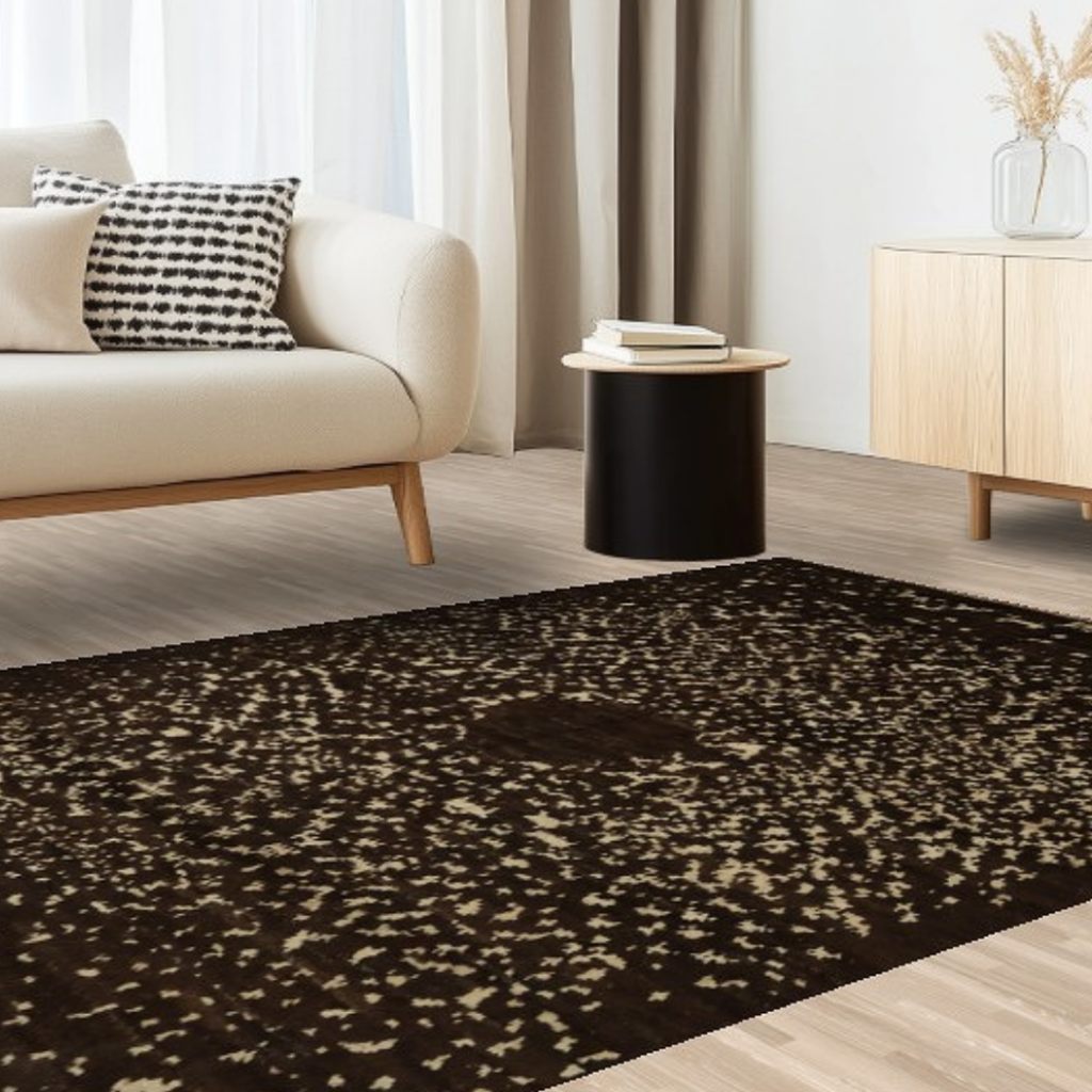 A minimalist living room with a beige sofa, patterned pillow, and a dark brown rug speckled with lighter beige tones, giving a textured look.