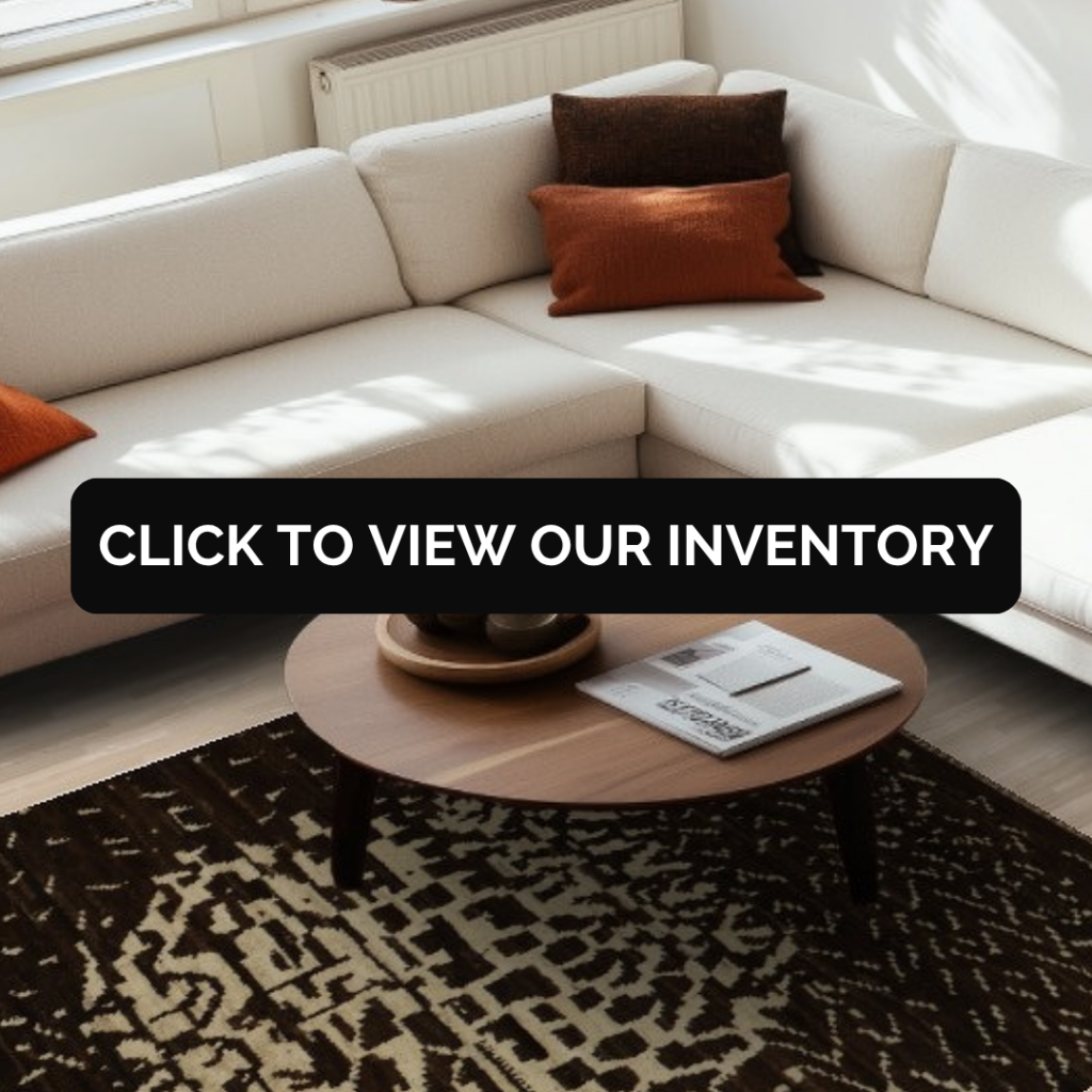 A modern living room with a cream sectional sofa, orange accent pillows, and a dark brown rug with an abstract beige pattern. The space feels warm and sunlit.