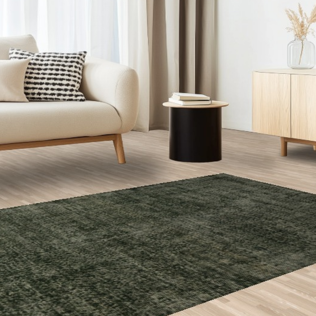 A serene modern living room with a beige sofa, light wood furniture, and a deep green rug with a subtle tonal texture laid over pale wood flooring.