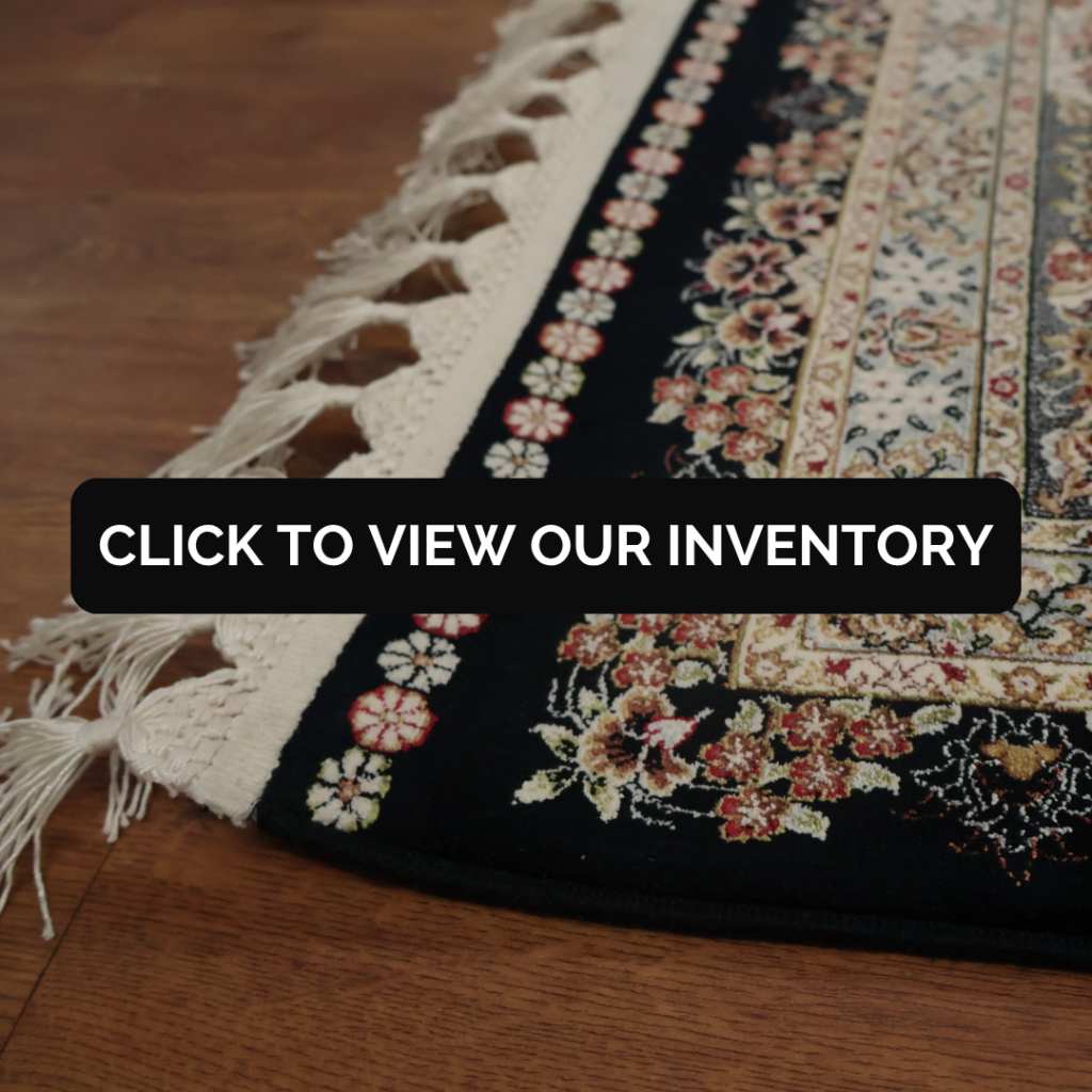 A close-up of a richly patterned rug with a black background, cream border, and detailed floral motifs. Decorative fringe lines one edge on a hardwood floor.