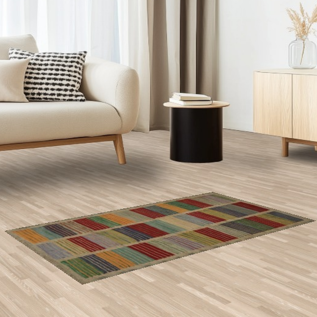 A close-up of a cozy living room with a cream-colored sofa, patterned pillow, and a rectangular rug in vibrant tones of red, green, and yellow on light wood flooring.