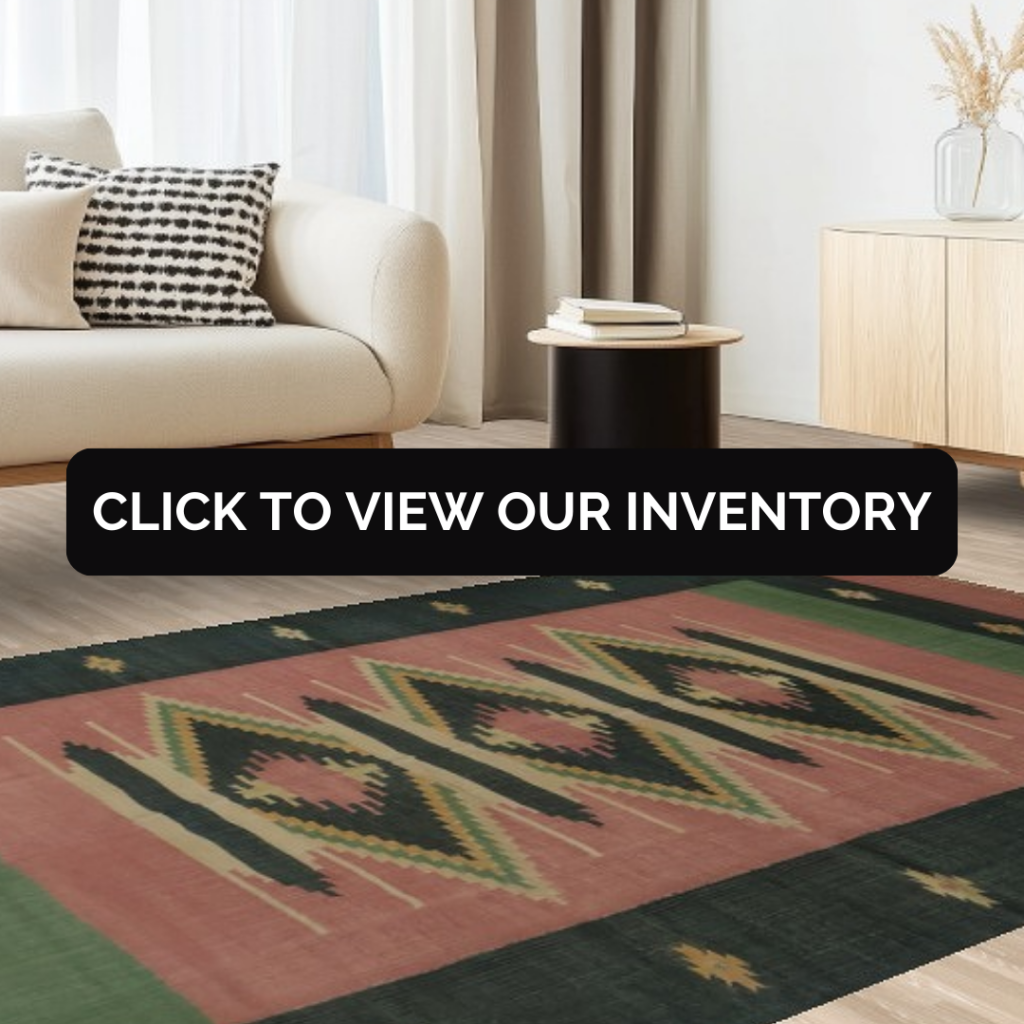 A spacious open living area features a teal velvet sofa and a glass coffee table positioned over a faded red patterned rug. The light wood floors and white kitchen create a clean, modern backdrop. Natural light brightens the entire space, giving it an inviting feel.