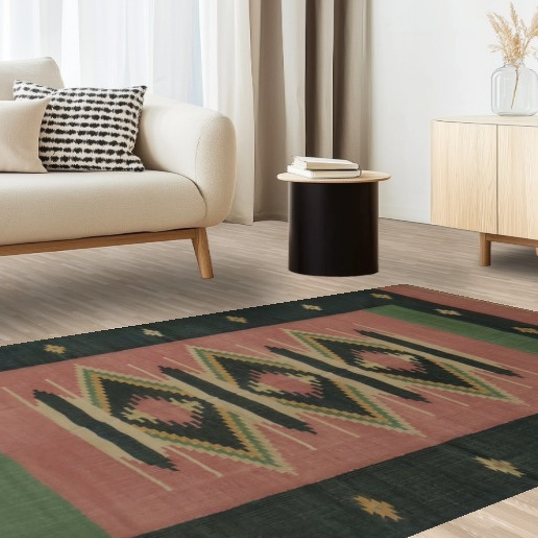 A cream sectional sofa with warm-toned throw pillows sits in a sunlit living room. A bold geometric rug in peach, black, and soft green tones extends beneath a round wooden coffee table. A large black button labeled “CLICK TO VIEW OUR INVENTORY” stretches across the center.