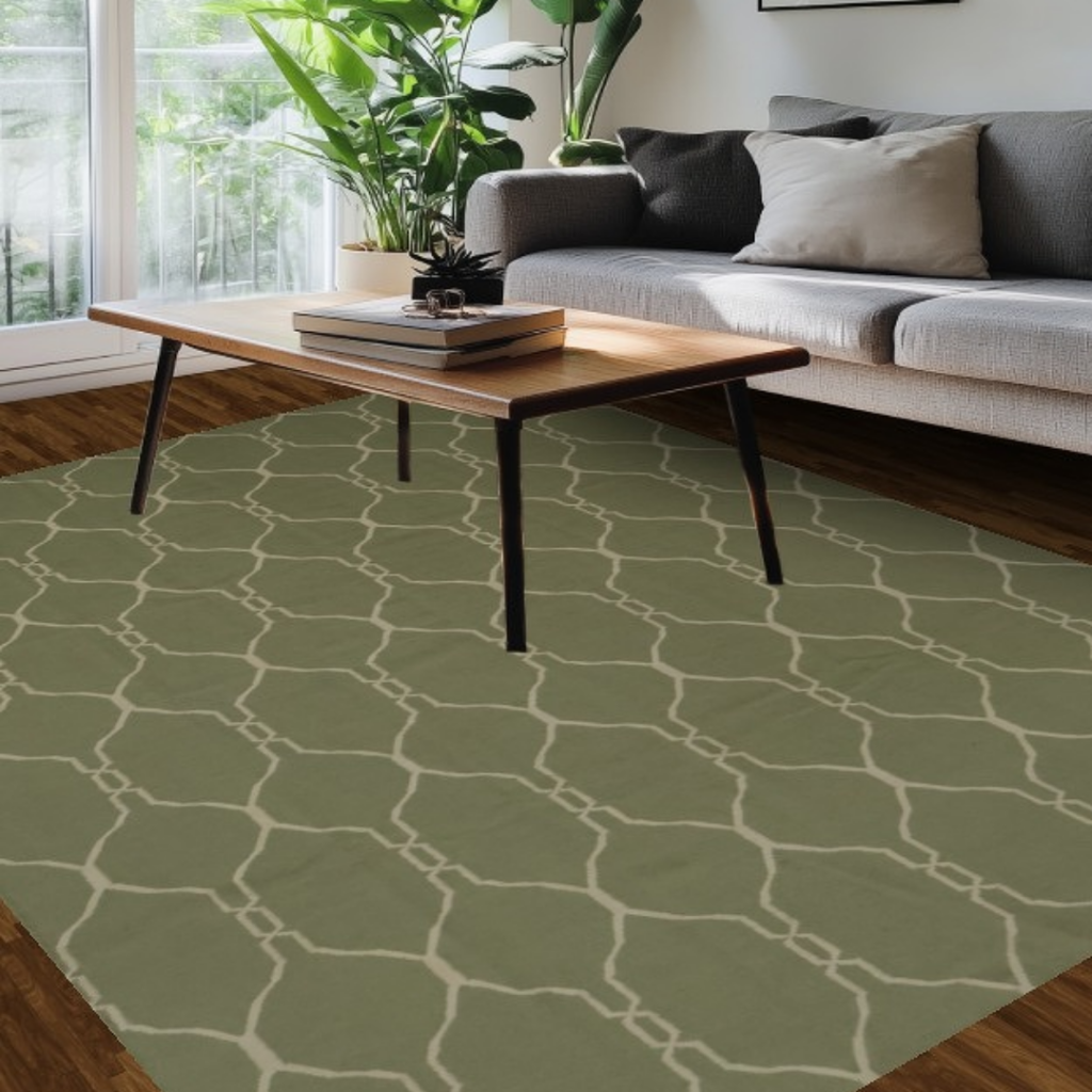 A bright living space with a gray sofa includes a long wooden coffee table resting on a sage-green rug with a repeating lattice pattern. Sunlight pours in through tall windows lined with plants. The warm wood floors and soft natural light create an inviting atmosphere.