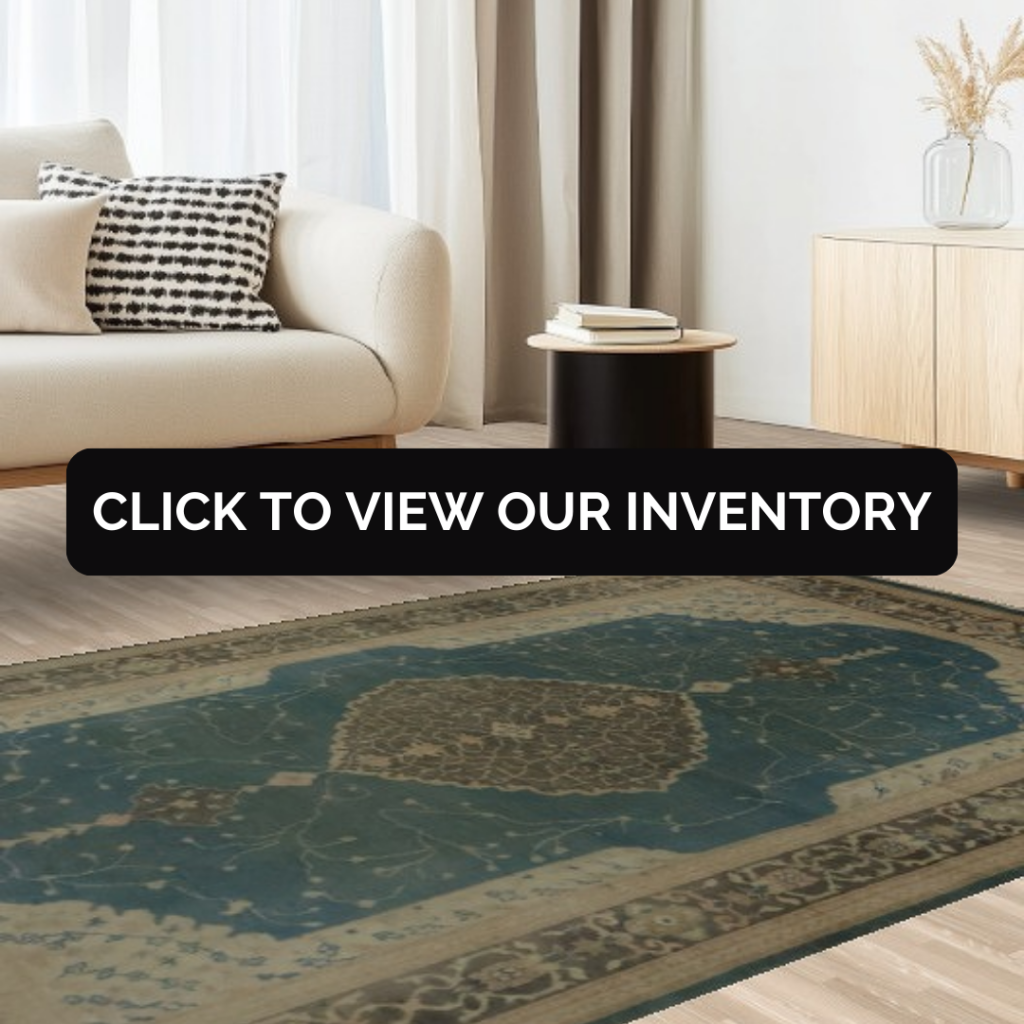 A cream-colored sofa sits beside light curtains and a small black side table topped with books. A large vintage-style rug in deep blue with tan and cream borders fills the foreground. A black “CLICK TO VIEW OUR INVENTORY” button is placed across the center.
