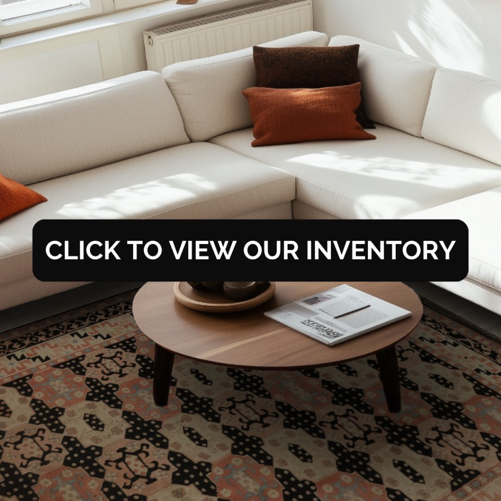 A warm, sunlit living room with a cream sectional is styled with earthy-toned throw pillows. A multicolored tribal-patterned rug in soft peach, black, and teal sits beneath a wooden coffee table. A black “CLICK TO VIEW OUR INVENTORY” button is centered across the scene.