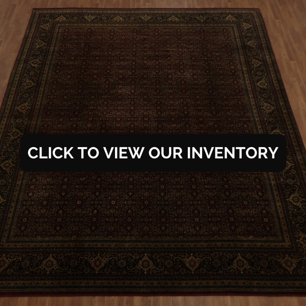 A large, dark-toned oriental rug with an intricate floral and geometric pattern sits on a hardwood floor. A bold black button with white text reading “CLICK TO VIEW OUR INVENTORY” is centered over the rug. The overall scene is simple and focused on the rug’s rich detailing.