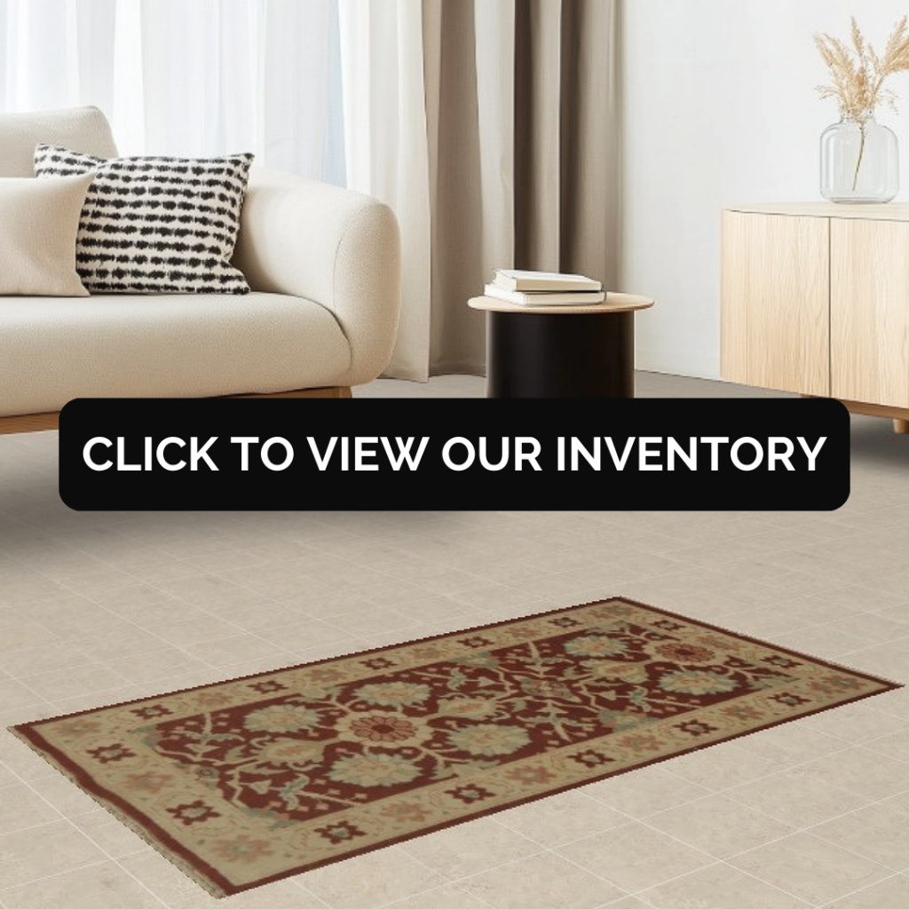 A neutral-toned living room features a cream sofa with a monochrome patterned pillow and a small black side table. A rectangular rug with a red and beige floral pattern lies on a tiled floor. A black “CLICK TO VIEW OUR INVENTORY” button overlays the center of the image.