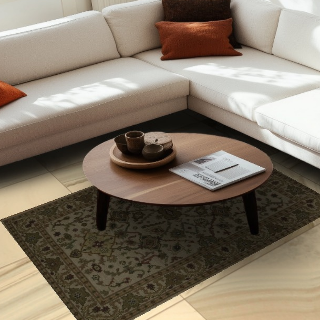 A cream-colored sectional sofa with rust and brown accent pillows sits in a softly sunlit living room. A dark green traditional rug with subtle floral detailing lies beneath a round wooden coffee table holding a tray and magazine. A black “CLICK TO VIEW OUR INVENTORY” button overlays the center.