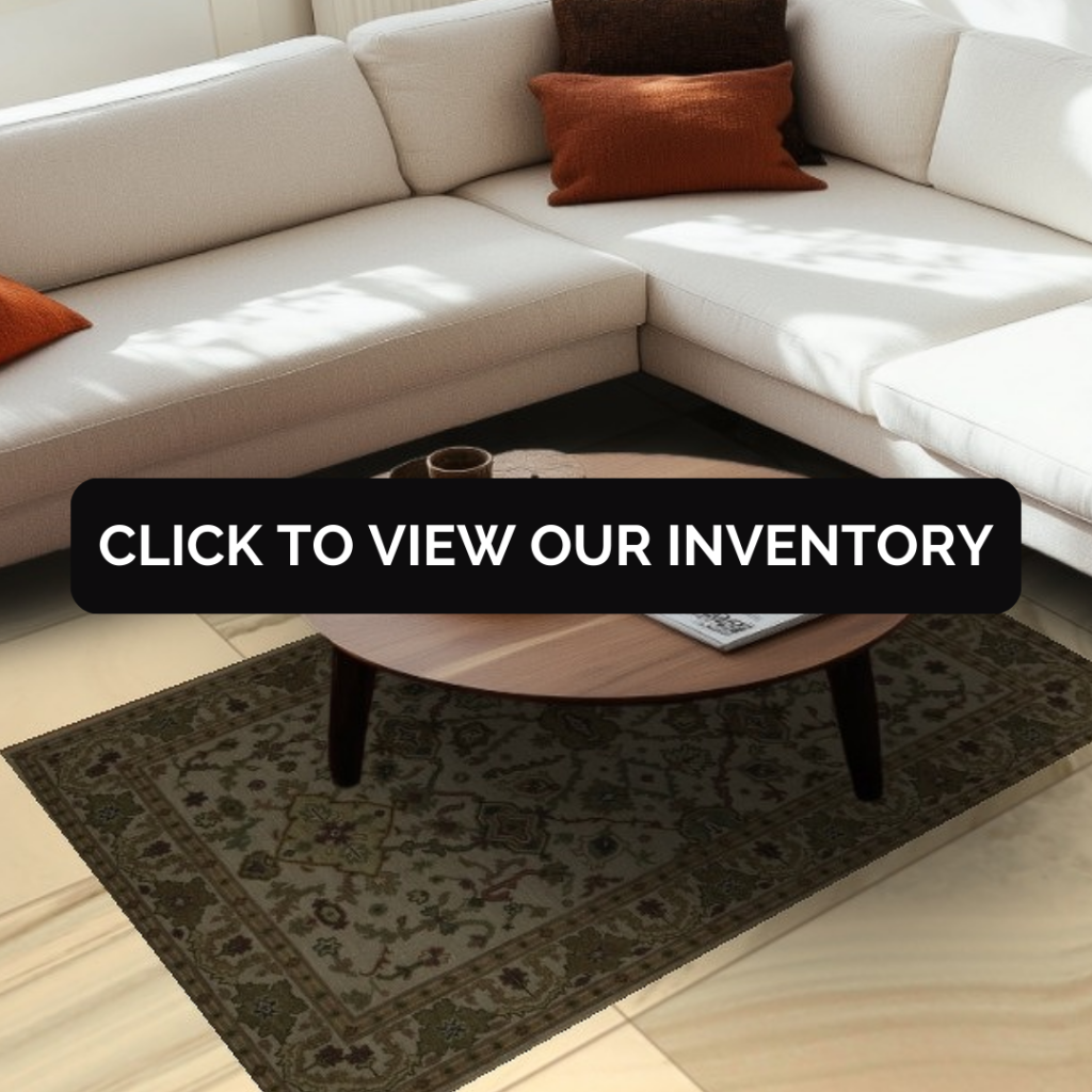 A cream-colored sectional sofa with rust and brown accent pillows sits in a softly sunlit living room. A dark green traditional rug with subtle floral detailing lies beneath a round wooden coffee table holding a tray and magazine. A black “CLICK TO VIEW OUR INVENTORY” button overlays the center.