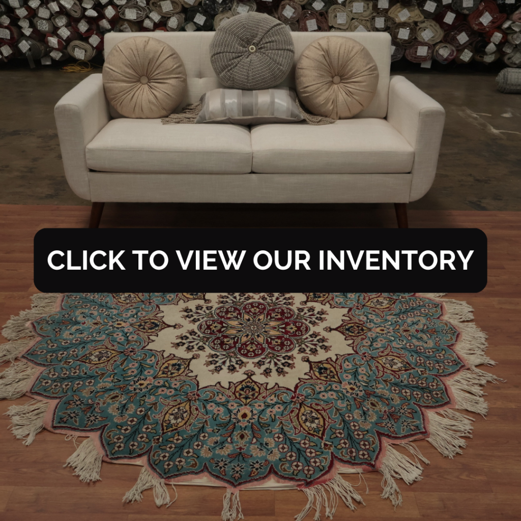 A cream-colored loveseat styled with round neutral throw pillows sits on a warm wood floor. In front of it is a round, ornate area rug with teal, ivory, and red floral patterns and decorative fringe.