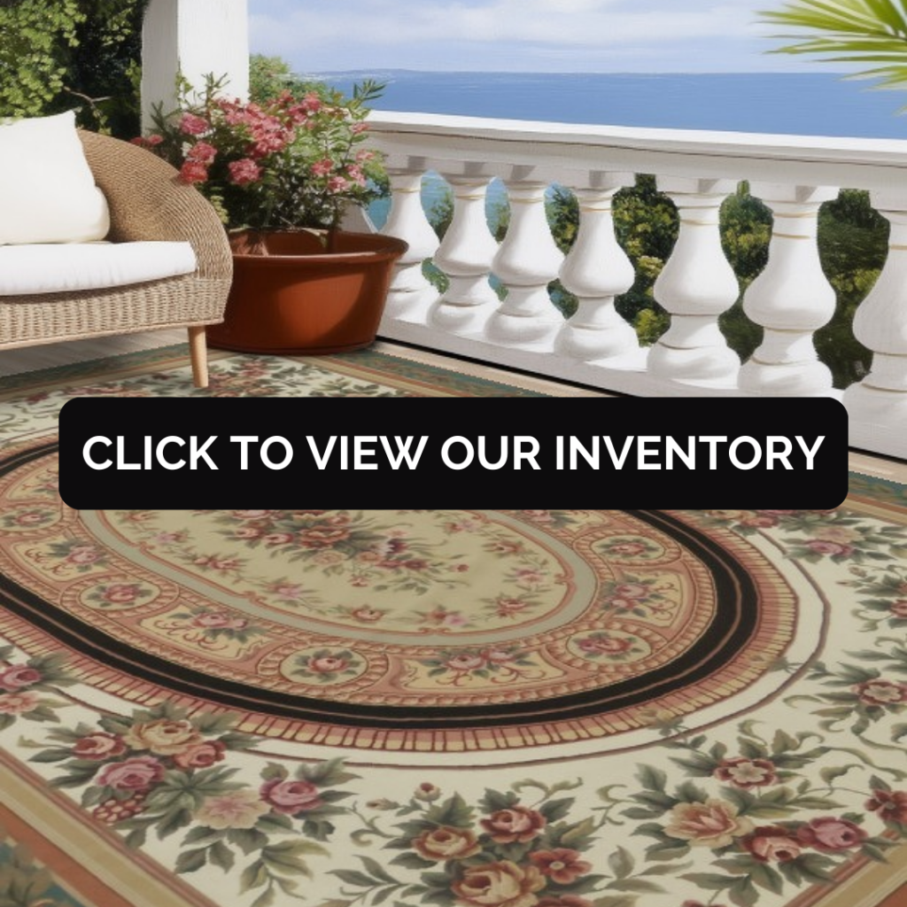 Outdoor patio scene featuring a floral oval area rug placed beneath wicker seating. A white balustrade overlooks greenery and water, creating a relaxed coastal setting.