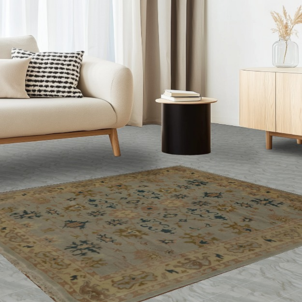 Minimalist living room with a neutral sofa, light wood furniture, and a muted vintage-style area rug. The rug features soft beige, olive, and blue patterns on a light stone floor.