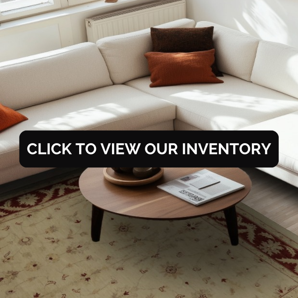 A bright living room featuring a cream sectional sofa accented with rust-colored throw pillows. A traditional patterned area rug in soft beige and red tones sits beneath a round wooden coffee table.