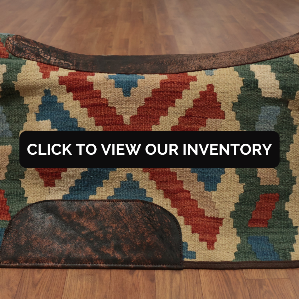 A close-up view highlights a saddle blanket with bold chevron-style geometric patterns in cream, red, teal, and forest green. Distressed dark brown leather trim lines the top edge, with a matching leather patch at the bottom. A black “CLICK TO VIEW OUR INVENTORY” button is centered across the design.