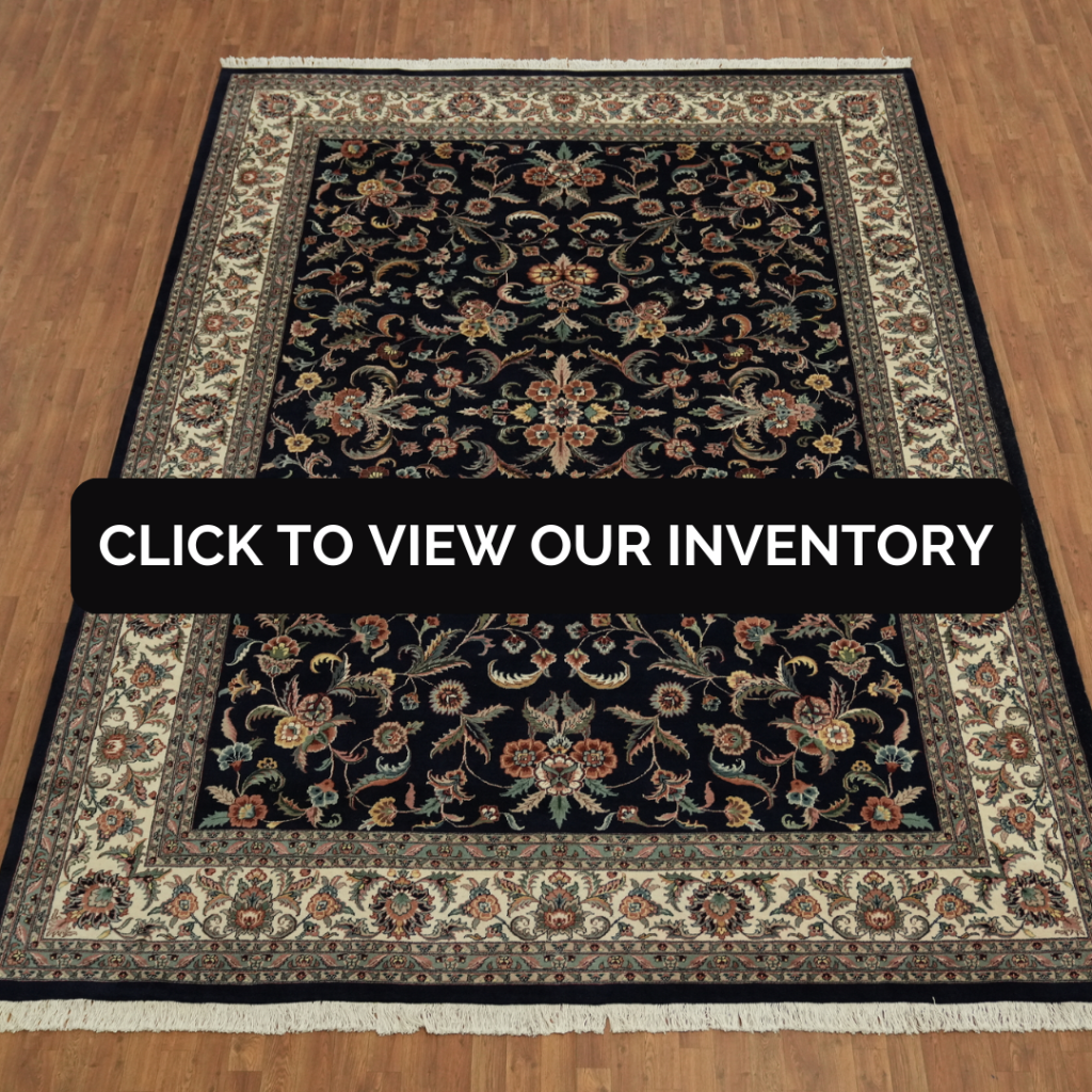 “Large rectangular area rug with dark navy background and floral border, displayed flat on a wood floor. Black button reads ‘Click to View Our Inventory.’”