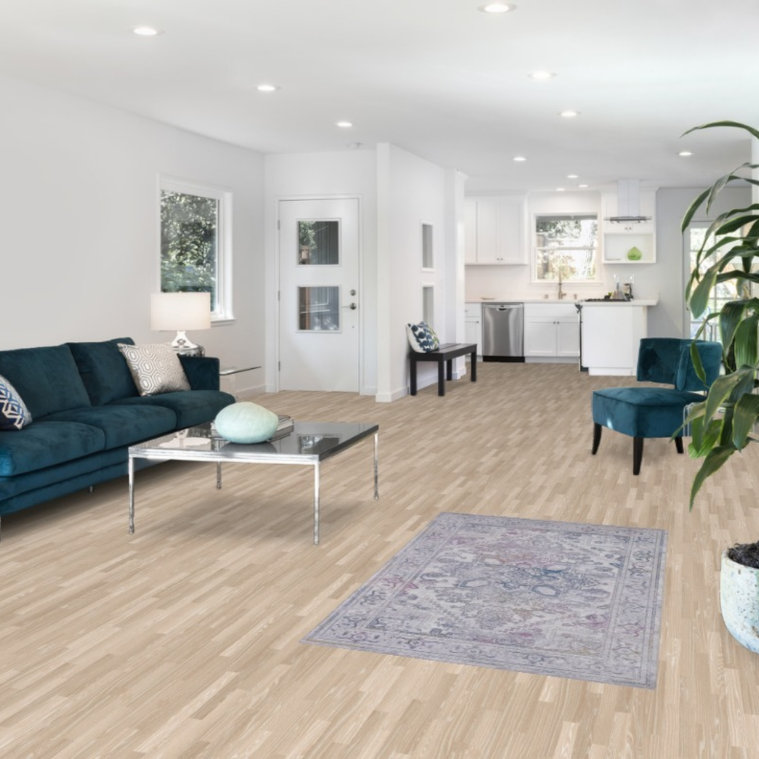 “Bright open living room with light wood floors, teal seating, and a small patterned area rug. Black button reads ‘Click to View Our Inventory.’”