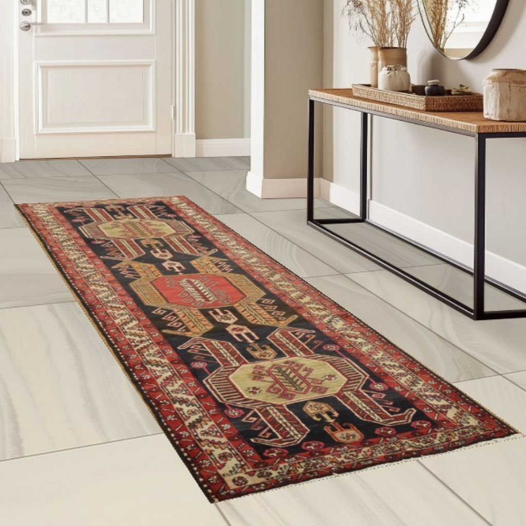 A red, navy, and cream tribal-style runner rug with geometric medallions is displayed along a hallway on light tile flooring. A wooden console table with decorative accents stands against the wall beside the runner.