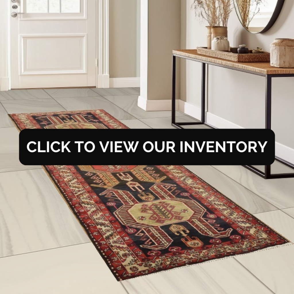 A long red and navy geometric runner rug with tribal-style medallions is placed in a bright entryway on light tile flooring. A console table with decorative vases and dried stems sits against the wall beside a white door. A black banner across the center reads, “CLICK TO VIEW OUR INVENTORY.”
