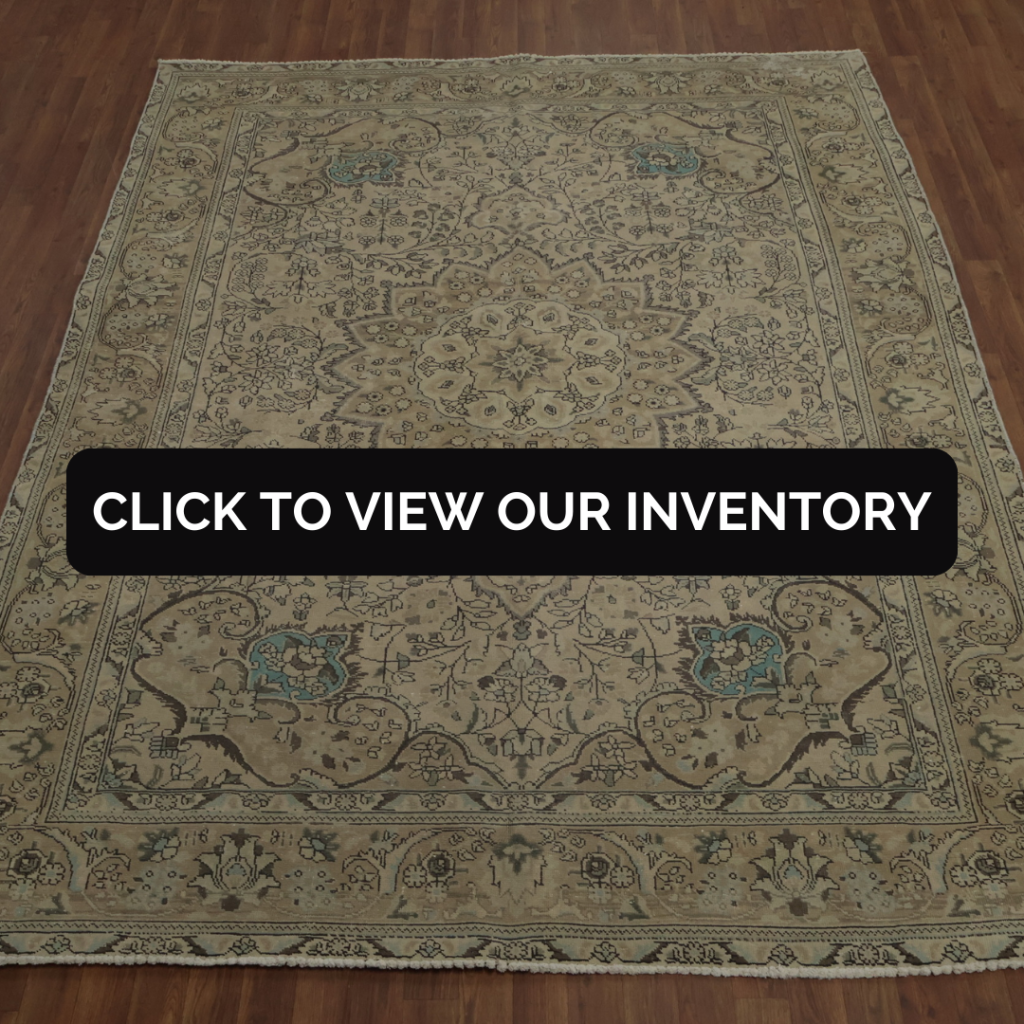 A beige traditional-style area rug with intricate floral and medallion patterns and small teal accents is displayed on a hardwood floor. A black banner across the center reads, “CLICK TO VIEW OUR INVENTORY.”
