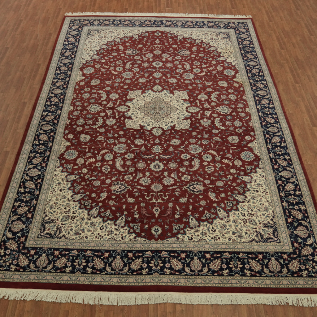A red Persian-style area rug with intricate floral patterns, a central medallion, and a navy border is laid out on a hardwood floor. The rug has cream fringe along the edges.