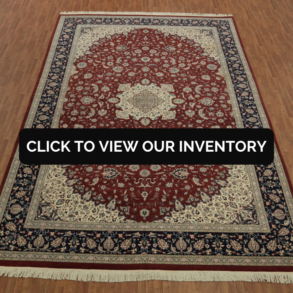 A large red Persian-style area rug with a detailed floral medallion and navy border is displayed on a hardwood floor. A black banner across the center reads, “CLICK TO VIEW OUR INVENTORY.”