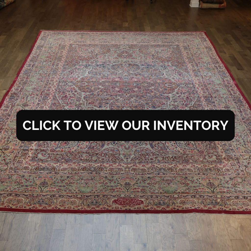 A traditional Persian-style rug with intricate floral patterns in red, cream, and blue tones displayed on a wooden floor. A black banner across the center reads “Click to view our inventory.”