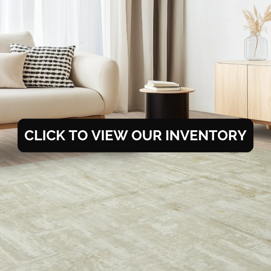 A minimalist living room with a cream sofa, black side table, and light wood cabinet, featuring a large neutral beige rug with subtle texture. A black banner across the center reads “Click to view our inventory.”