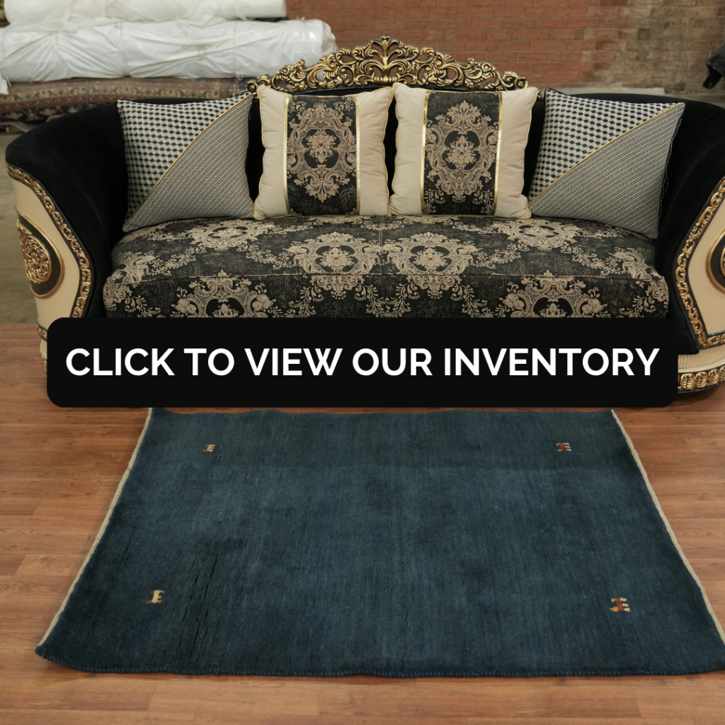 An ornate black and gold sofa with intricate carved details and patterned cushions sits behind a deep blue rug with minimal accents. A black banner across the center reads “Click to view our inventory.”