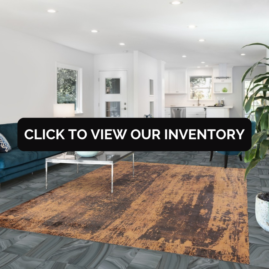 A spacious open-concept living room with white walls, a teal sofa, and a large distressed-style area rug in warm brown tones. A black banner across the middle reads “Click to view our inventory.”