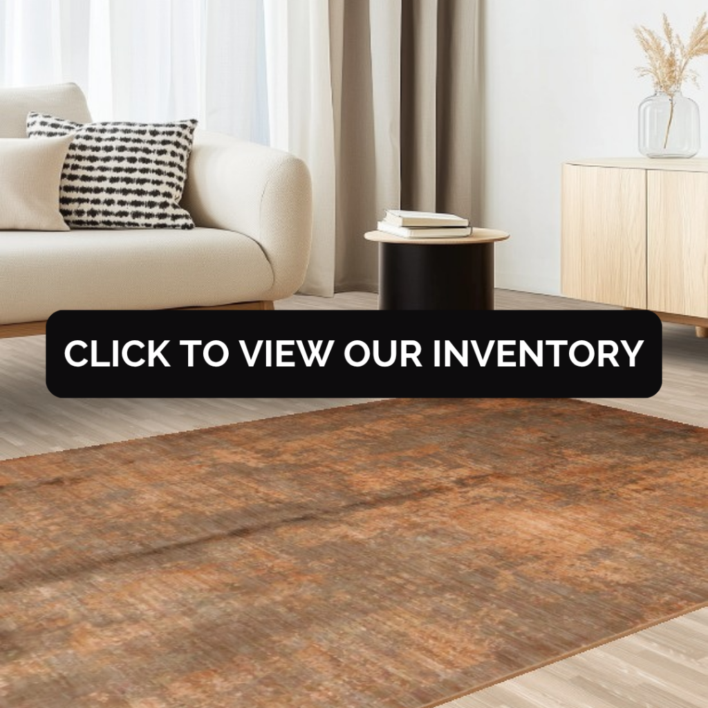 A modern living room with a cream sofa and minimalist decor, featuring a large distressed brown rug with subtle tonal variations. A black banner across the center reads “Click to view our inventory.”