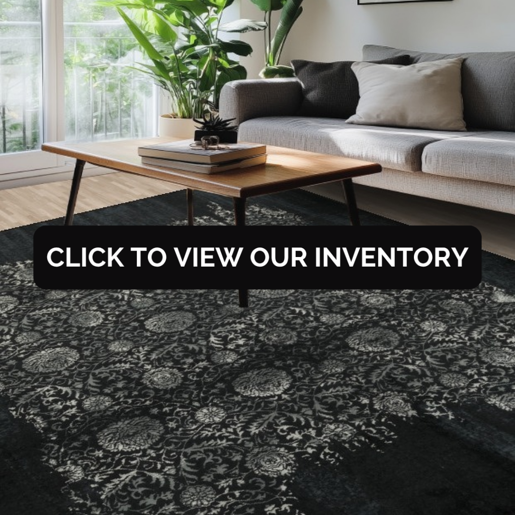 A bright, modern living room with a gray sofa, wooden coffee table, and leafy plants by a window, featuring a dark patterned rug. A bold black banner across the center reads “Click to view our inventory.”